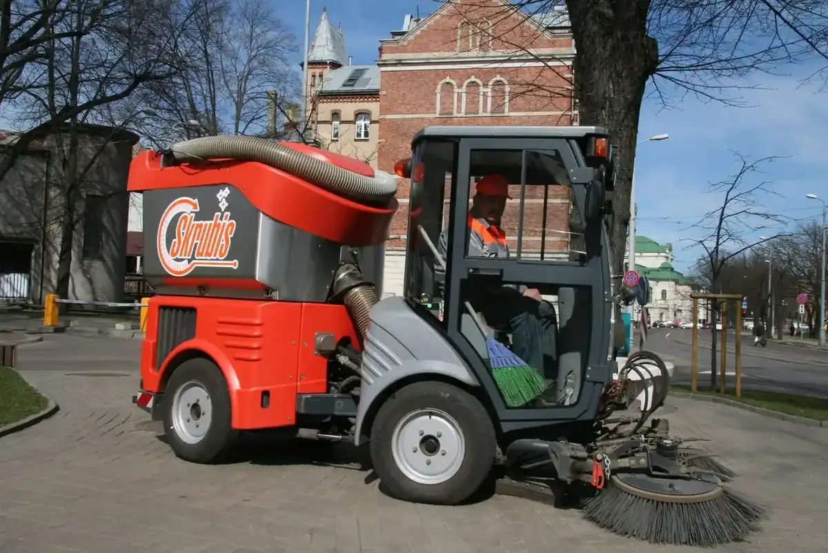 Skrubis ielu slaucējs ar operatoru kabīnē uzkopj ietvi Rīgas centrā