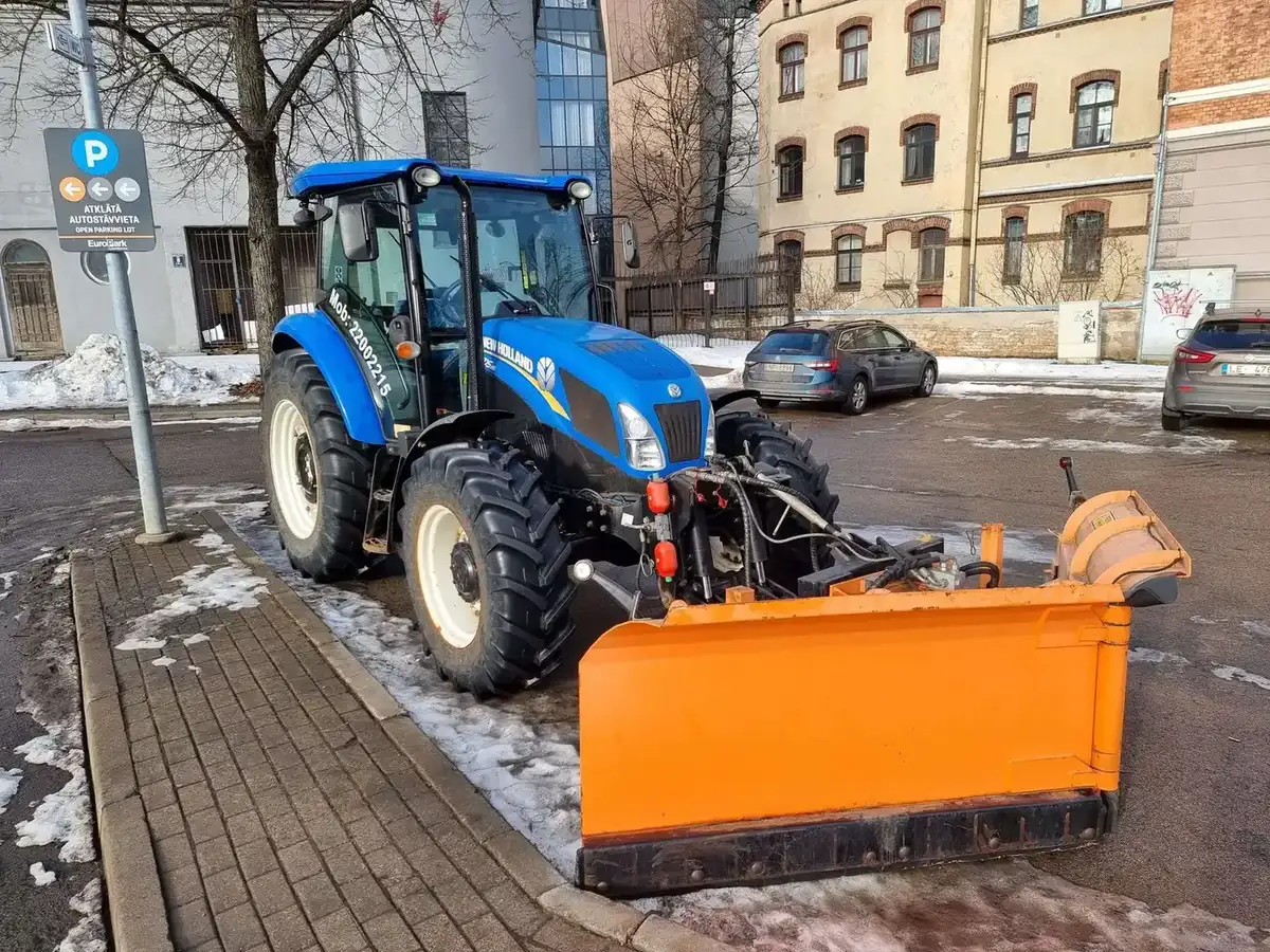 Traktors ar oranžu sniega lāpstu tīra EuroPark autostāvvietu Rīgas centrā